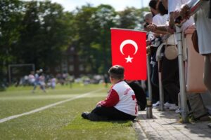 Kleine Kinder mit einer Türkei-Fahne schauen beim Spiel des Türkischen SV Lübeck gegen TSB Flensburg II auf dem Sportplatz zu.